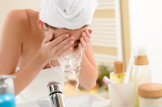 Rostro de mujer salpicando con agua sobre el lavabo del baño